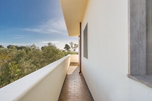 A narrow corridor with a tiled floor leading to a balcony with a view of trees and sky.