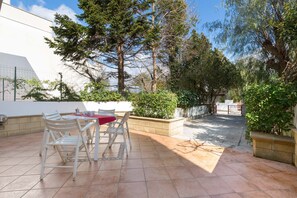 Eine Terrasse mit Tisch und Stühlen, umgeben von Grünpflanzen und Bäumen.