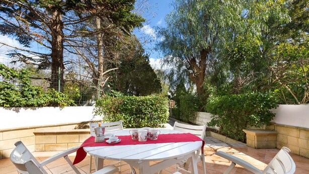 An outdoor patio with a white table set for dining, surrounded by white chairs, and a red tablecloth. - Villetta Amilcare (Lecce)