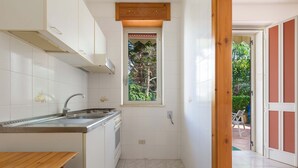 A compact kitchen with white cabinets, a stainless steel sink, and a window with a view of greenery. - Villetta Amilcare (Lecce)