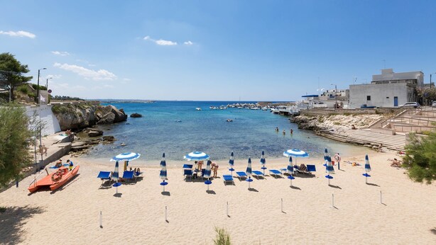 Une plage avec une eau d’un bleu limpide, un bateau et plusieurs parasols.