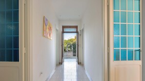Un couloir au sol carrelé de carreaux blancs, un tableau accroché au mur de gauche et une porte avec des panneaux de verre bleus sur le côté droit.