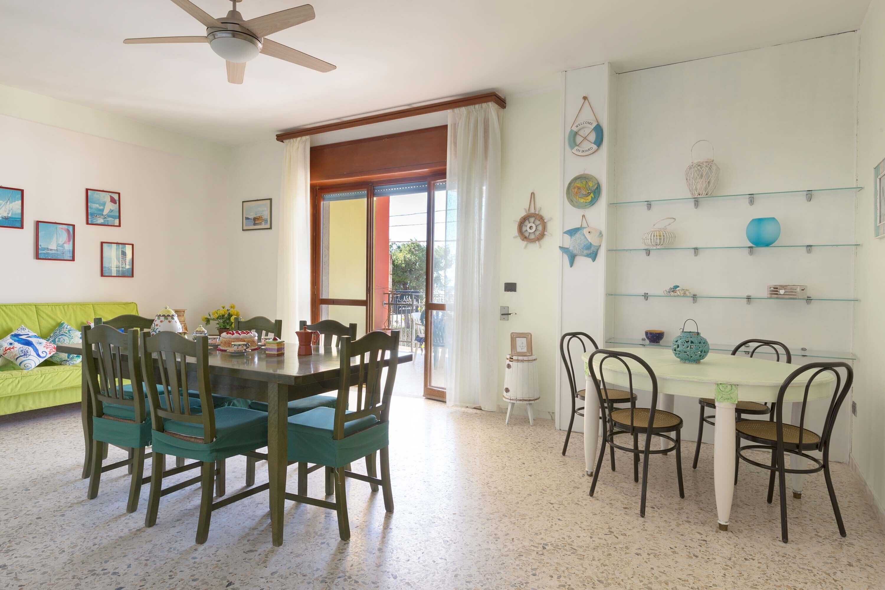 A dining area with a table and chairs, a ceiling fan, a green sofa, and a door leading outside.