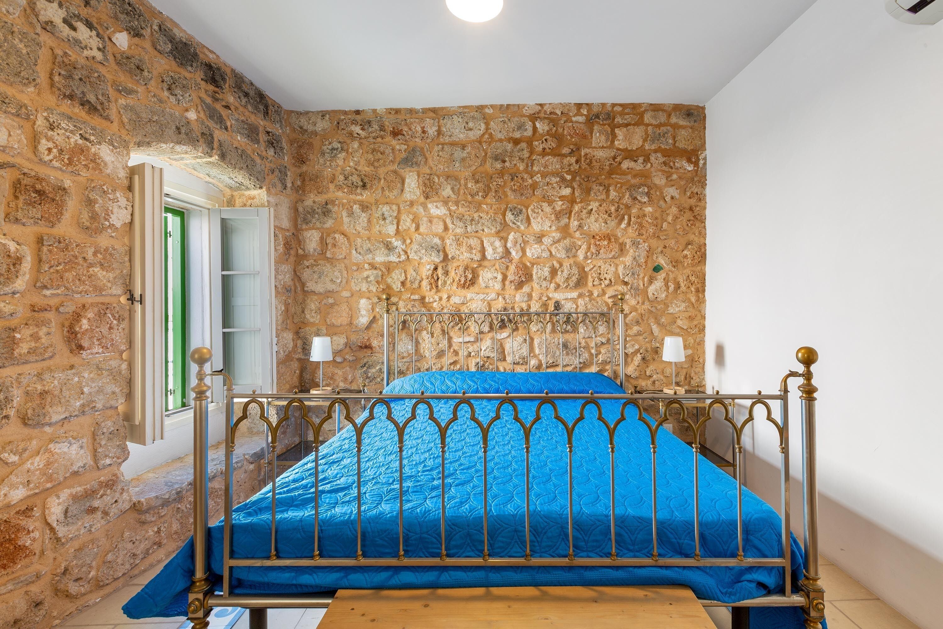 A room with a stone wall, a bed with a metal frame, and a wooden table.