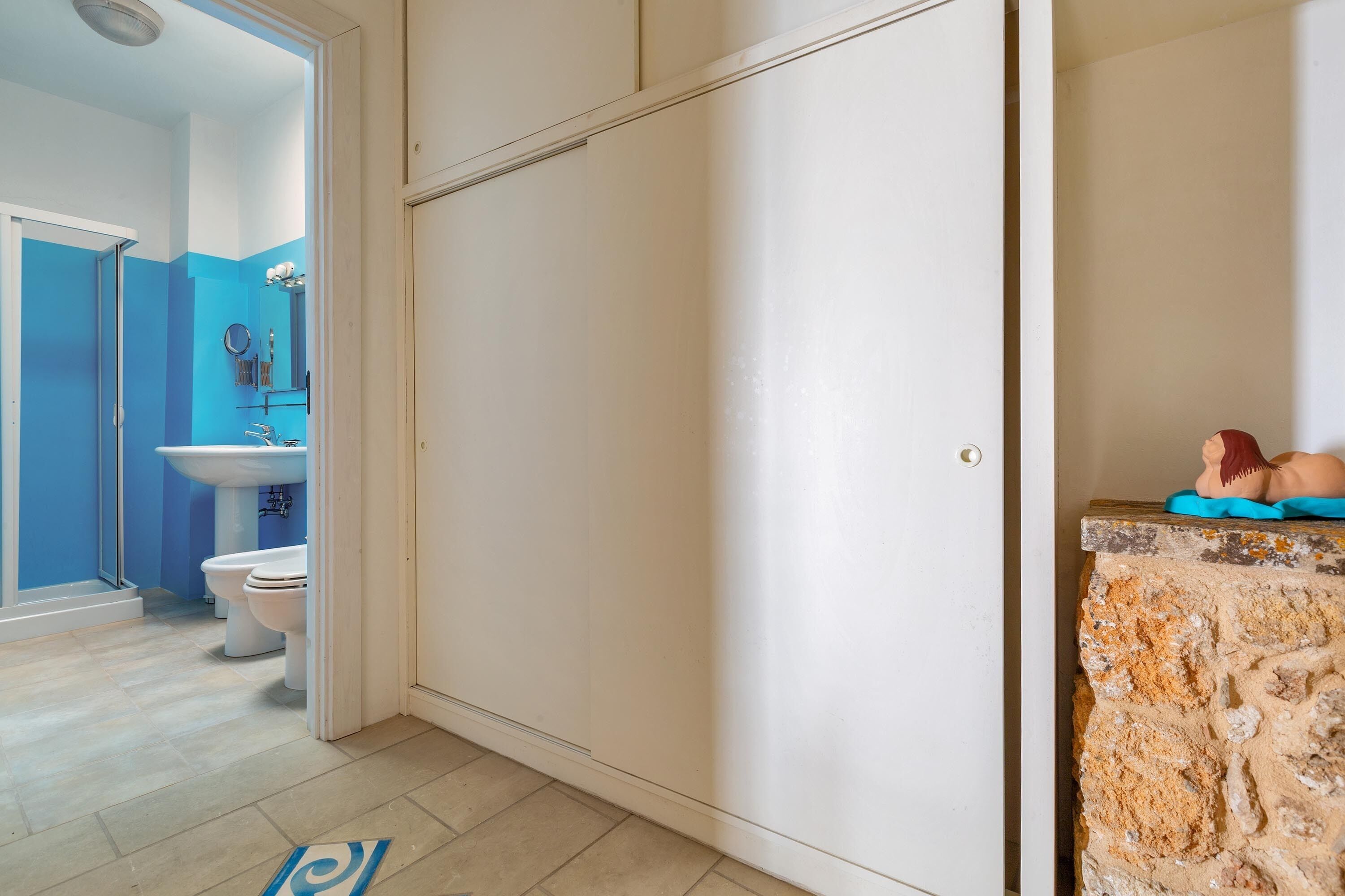 Un bagno con il water bianco, pareti azzurre, un lavandino e uno specchio.