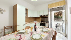 A dining area with a table set for four, a wine bottle, and a kitchen in the background. - Appartamento Baiabella (Gallipoli)