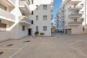 A courtyard with a paved area, potted plants, and a building with multiple balconies and windows.