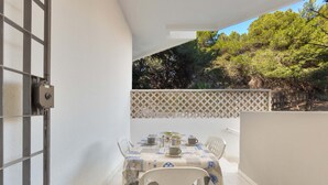 A balcony with a table set for two, chairs, and a view of trees and sky. - Appartamento Baiabella (Gallipoli)