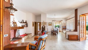 A spacious living room with a wooden bench, a dining area with a table and chairs, and a kitchen area with a counter and cabinets. - Villa Alice (Porto Cesareo)