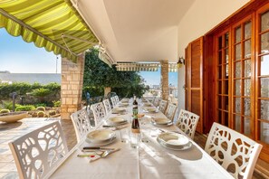 A dining area with a long table set for a meal, surrounded by white chairs, under a green awning. - Villa Alice (Porto Cesareo)