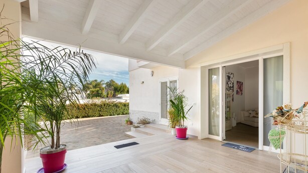 A covered patio with wooden flooring, potted plants, and a sliding glass door leading to an interior room. - Aria di Barocco (Carmiano)