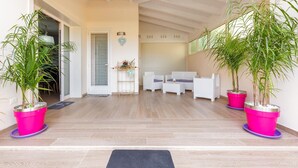 A spacious indoor area with a wooden floor, white furniture, and two large potted plants. - Aria di Barocco (Carmiano)