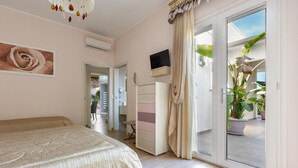 A bedroom with a bed, a dresser, a TV, and a sliding glass door leading to a balcony with plants. - Aria di Barocco (Carmiano)