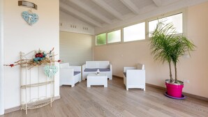 A room with a white sofa set, a small table, a decorative metal shelf, and a large potted plant. - Aria di Barocco (Carmiano)