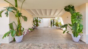 A covered walkway with potted plants, a bicycle, and a door leading to another area. - Aria di Barocco (Carmiano)