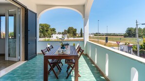 En balkon med et bord og stole, udsigt over landskabet, samt en dør der fører til et andet rum.