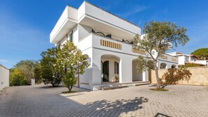 En modern villa med en stenlagd innergård, vit fasad och flera balkonger.