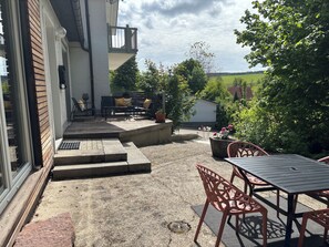 Um pátio com mobiliário de exterior, uma pequena mesa e degraus que levam a uma varanda.