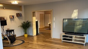 A modern living room with wooden flooring, a flat-screen TV, a potted plant, and a small table with a lamp. - Beautiful and cozy house in the middle of nature. (Niedereschach)
