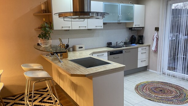 A modern kitchen with a central island, white cabinets, a stainless steel range hood, and a patterned rug. - Beautiful and cozy house in the middle of nature. (Niedereschach)