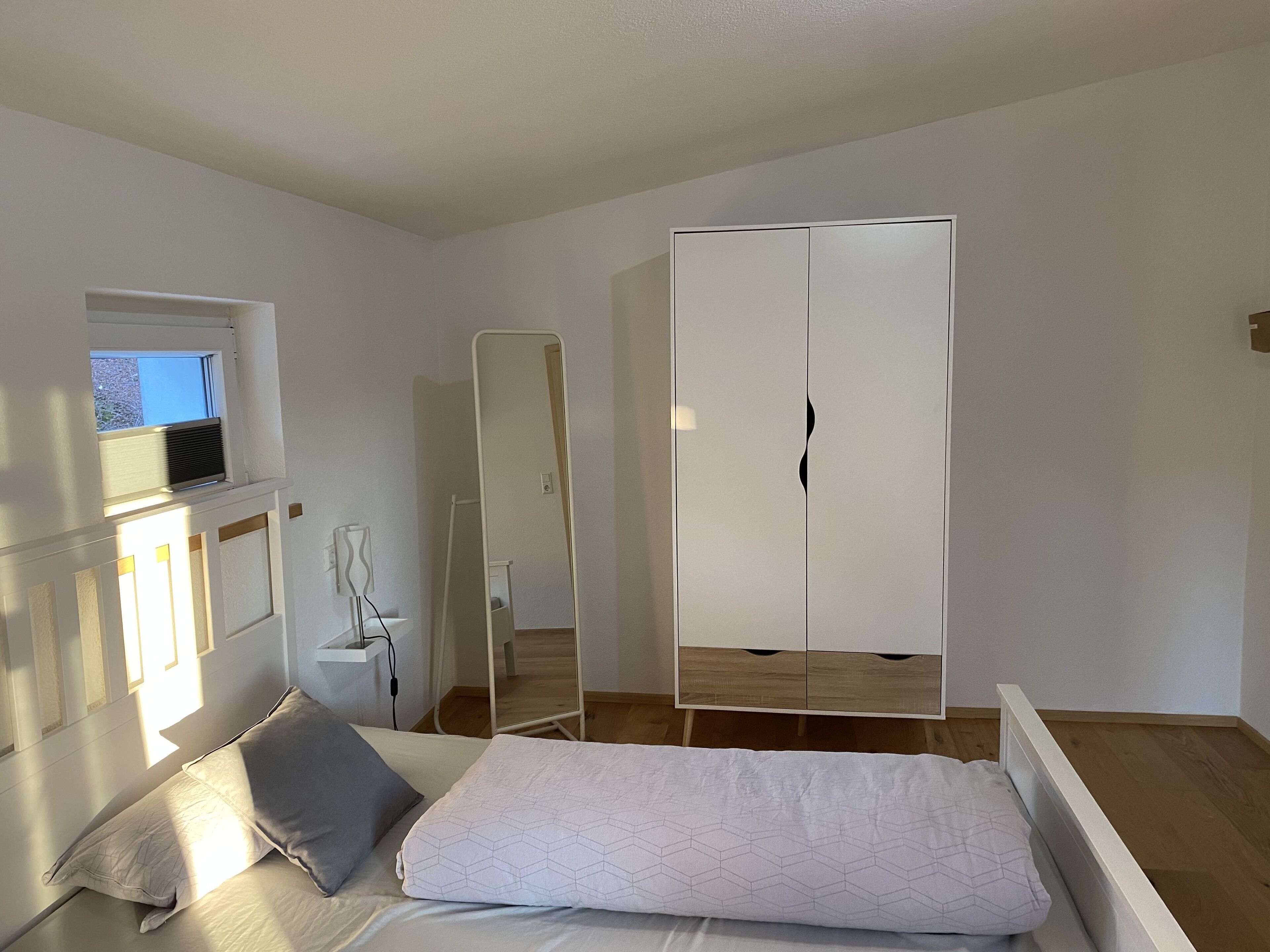 A bedroom with a bed, a wardrobe, a window, and a mirror.