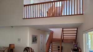 A spacious living room with a high ceiling, a wooden staircase, a sofa, a lamp, and a framed picture on the wall. - LUXURIOUS FIVE BEDROOM FLORIDA ESCAPE (Port Charlotte)
