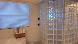 A bathroom with a glass shower enclosure, a bathtub, a window with blinds, and a wicker basket with towels. - LUXURIOUS FIVE BEDROOM FLORIDA ESCAPE (Port Charlotte)