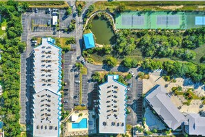 An aerial view of a hotel with multiple parking lots, a tennis court, and a swimming pool.