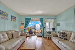 A living room with two beige sofas, a wooden coffee table, a small white table, and a chair. There are curtains, a lamp, and a window with a view of the sky. - Savannah Beach & Racquet Club 303A (Tybee Island)