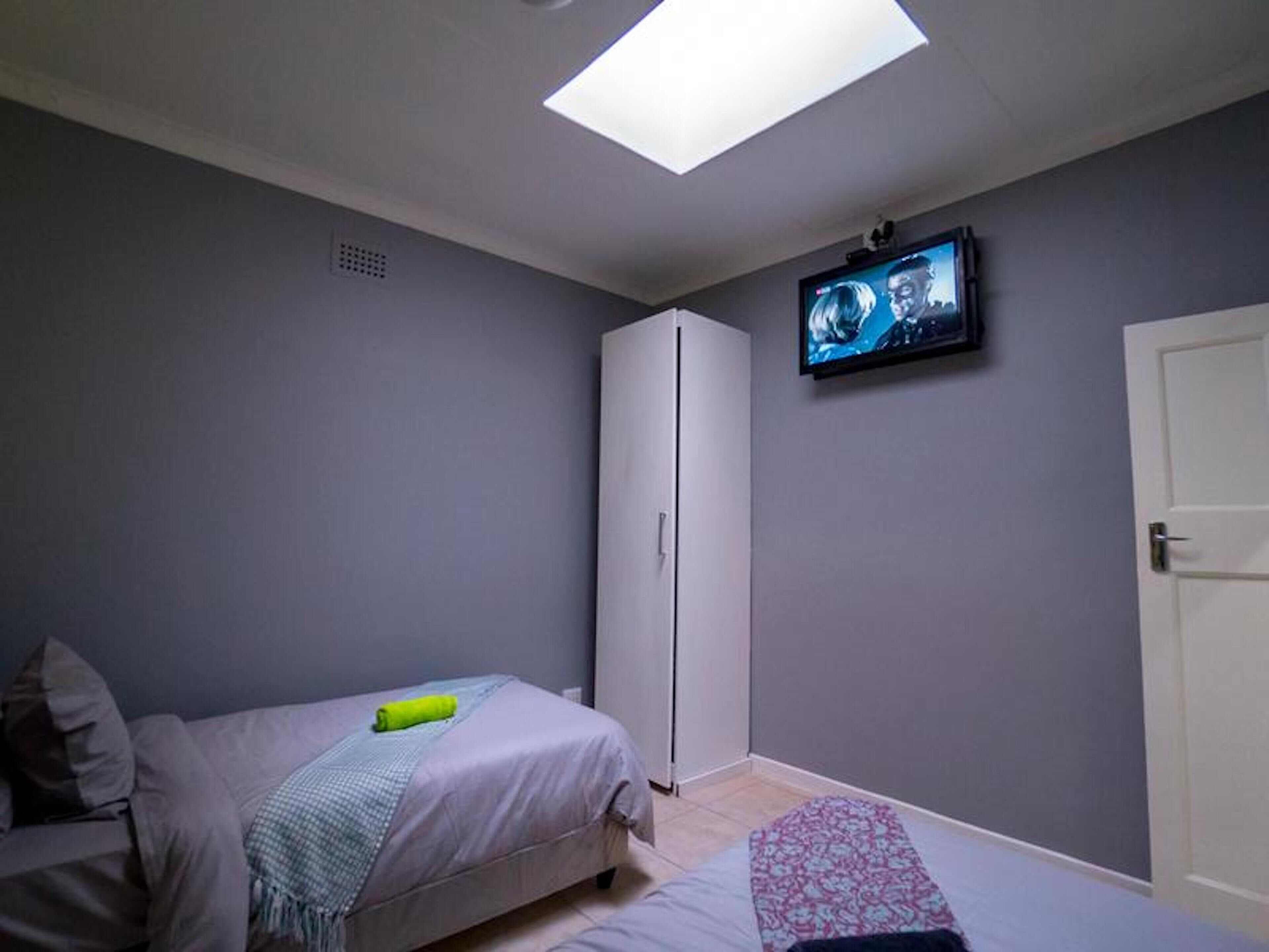 A bedroom with a bed, a wardrobe, a television on the wall, and a skylight.