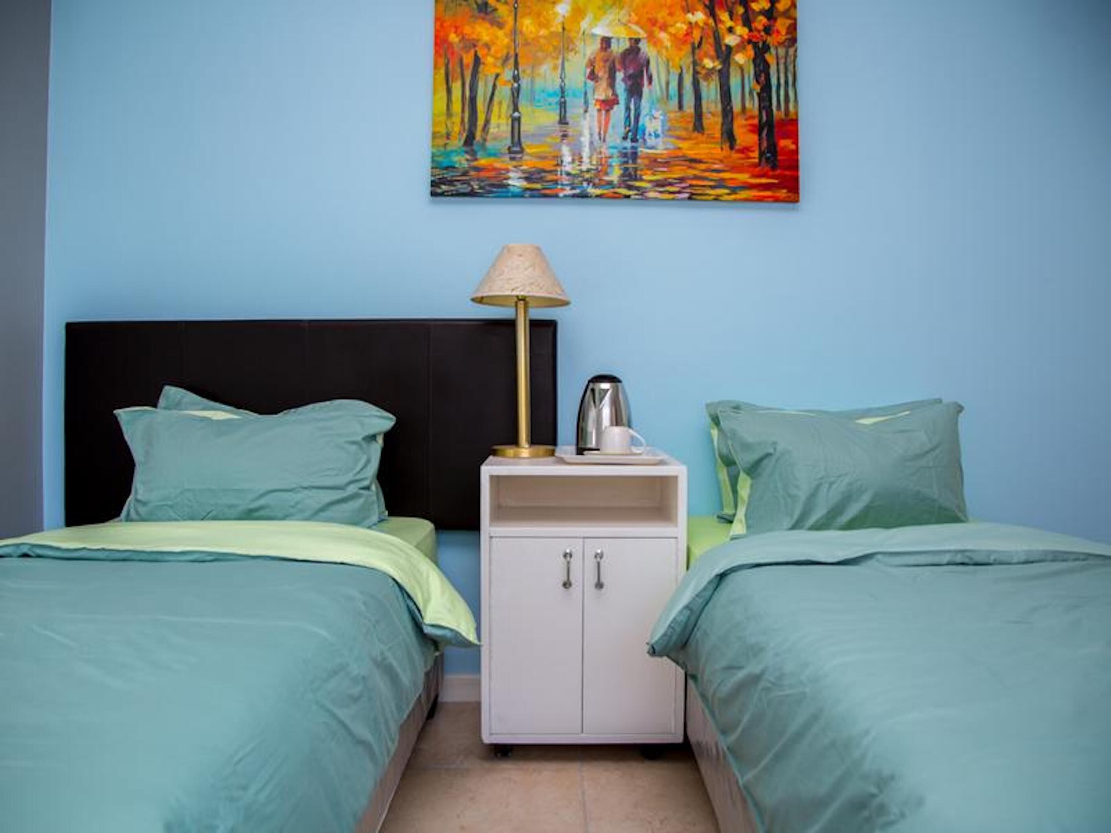 Une chambre avec deux lits, une table de chevet, une lampe et un tableau au mur.