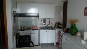 Una cocina compacta con alacenas blancas, una estufa, un fregadero y una pequeña encimera.