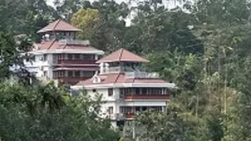A multi-story building with a red roof, surrounded by dense greenery.