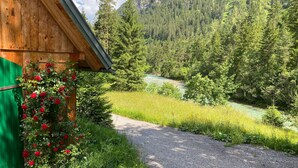 Une cabane en bois, avec un chemin de gravier menant à une rivière bordée d’une forêt dense.