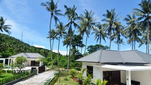 A modern resort with two white buildings, a paved walkway, and a lush garden with palm trees. - Lombok From Your Private Villa Sepuluh (Senggigi)