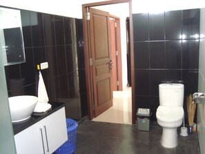 Une salle de bain avec un lavabo blanc, un panier bleu, des toilettes blanches et un balai.