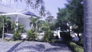 A modern building with a covered patio area, surrounded by palm trees and other tropical vegetation. - Lombok From Your Private Villa Sepuluh (Senggigi)