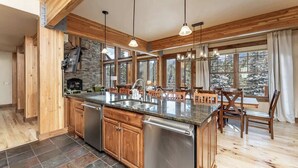 A spacious kitchen with wooden cabinets, a large island, stainless steel appliances, and pendant lighting. - Moose Creek | Ski-In/Out + Hot Tub (Big Sky)