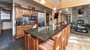 A modern kitchen with wooden cabinets, granite countertops, and a central island with bar seating. - Moose Creek | Ski-In/Out + Hot Tub (Big Sky)