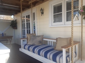 A porch with a swing seat, white railings, and a hanging planter. - Harbour View Cottage Boutique B&b (Auckland)