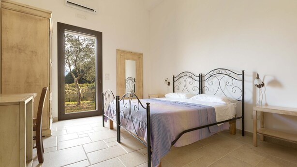 Un dormitorio con una cama, un escritorio y una silla. Hay una puerta que da a un balcón.