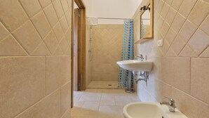 Un baño con azulejos color beige, una ducha con cortina azul estampada, un lavabo y un espejo.