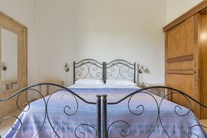 Un lit avec un cadre en métal et une couvre-lit à motifs, une armoire en bois et un miroir au mur.