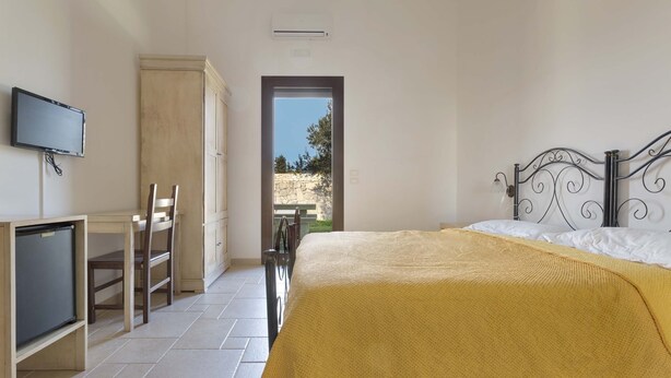 Un dormitorio con cama, escritorio con televisor, armario y vista al exterior.