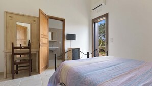 Un dormitorio con cama, armario de madera, una silla, televisión y baño visible a través de una puerta abierta.