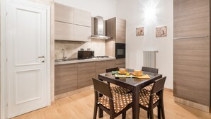 Cozinha compacta com armários de madeira, forno embutido e mesa de jantar com cadeiras.