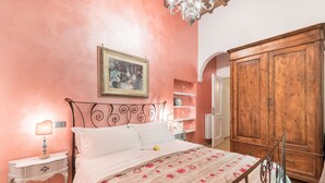 Quarto com cama, mesas de cabeceira, guarda-roupa e lustre.