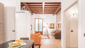 Uma sala de estar moderna com teto de madeira, uma área de jantar com mesa de vidro e um sofá com almofadas laranja.