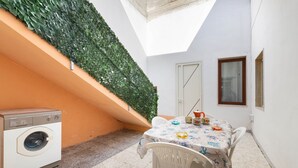 Un pequeño lavadero con lavadora, una mesa con sillas y una pared verde.