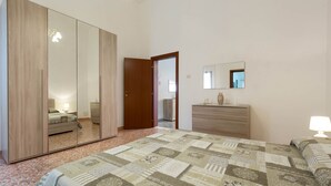 Un dormitorio con un armario grande, una cama con colcha estampada, un aparador y un espejo en la pared.